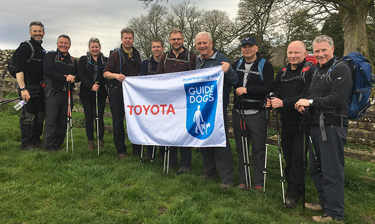 The Toyota GB Directors pose in the countryside holding a Toyota and Guide Dogs flag.