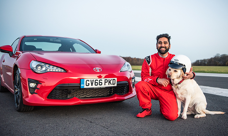 Dr Amit Patel and his guide dog, Kika, sit in front of a red Toyota GT86,