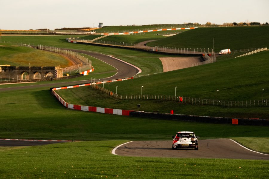 A Toyota Corolla touring car races downhill at Donington Park race circuit. The circuit winds off into the distance.